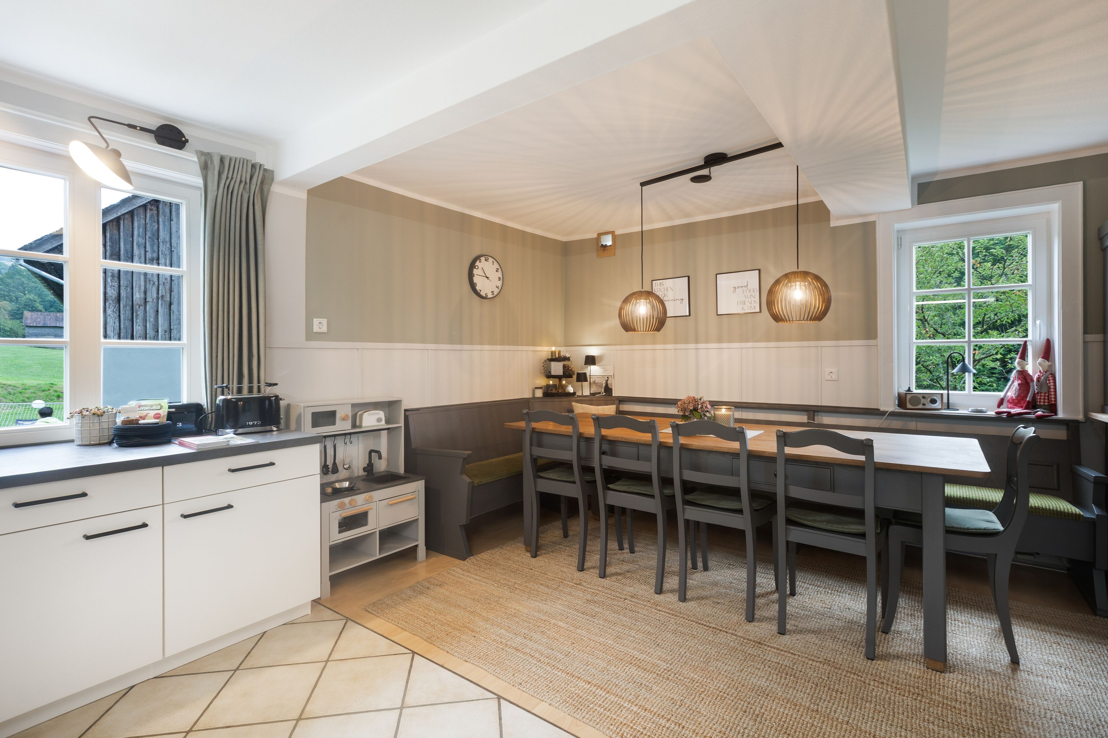 Een moderne keuken met een eethoek, voorzien van een inbouwoven, een spoelbak en een raam met uitzicht op groen.