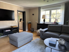 A living room with a sofa, ottoman, TV, and a lamp on a table.