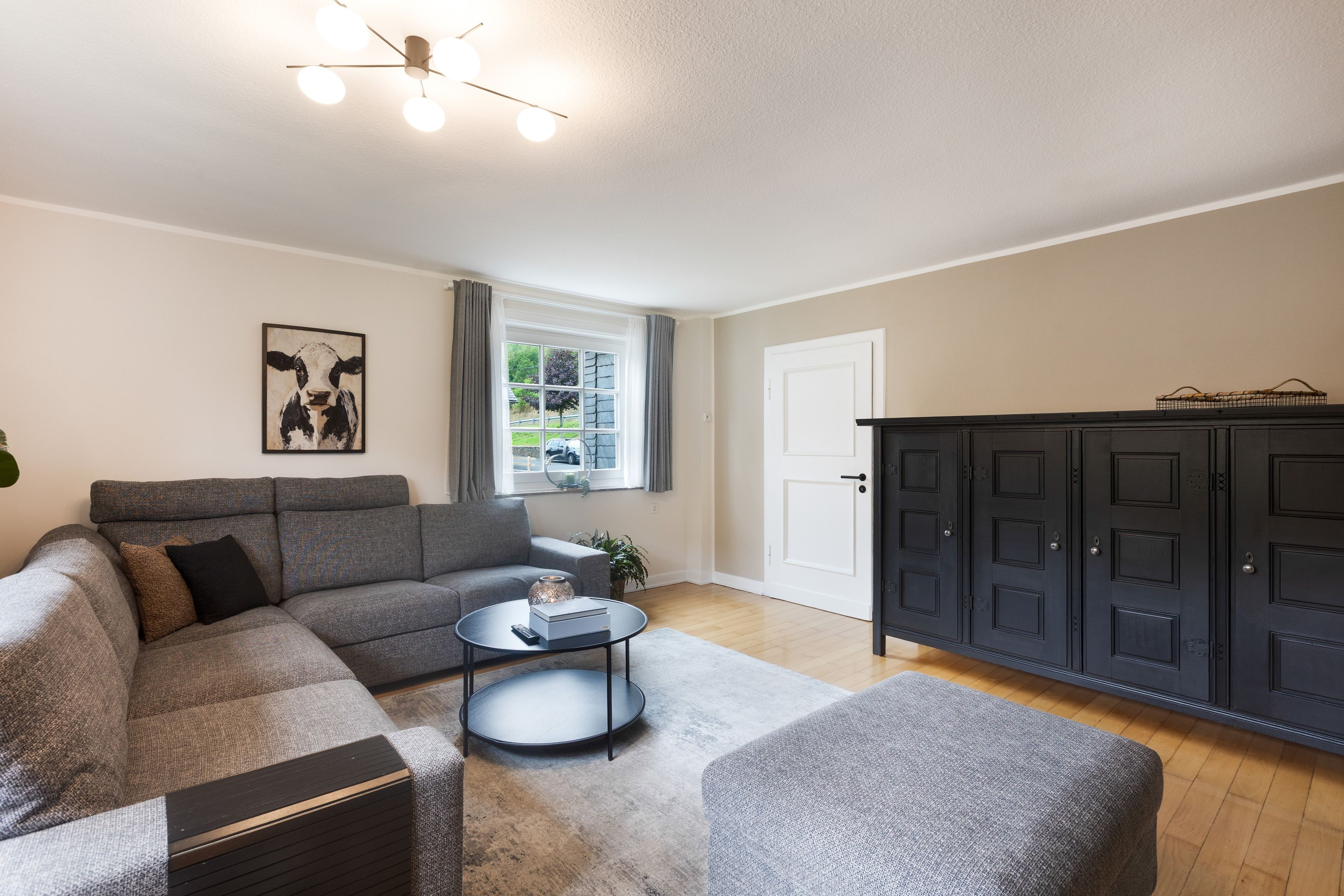 A living room with a grey sofa, a round coffee table, a black cabinet, and a painting on the wall.