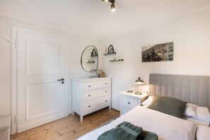 Un dormitorio con cama, mesita de noche, lámpara, cómoda, espejo y un cuadro en la pared.