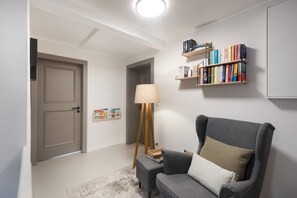 A room with a grey armchair, a floor lamp, a bookshelf, and a door.