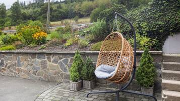 Uma cadeira suspensa de vime com almofada, colocada em uma parede de pedra com vista para o jardim.