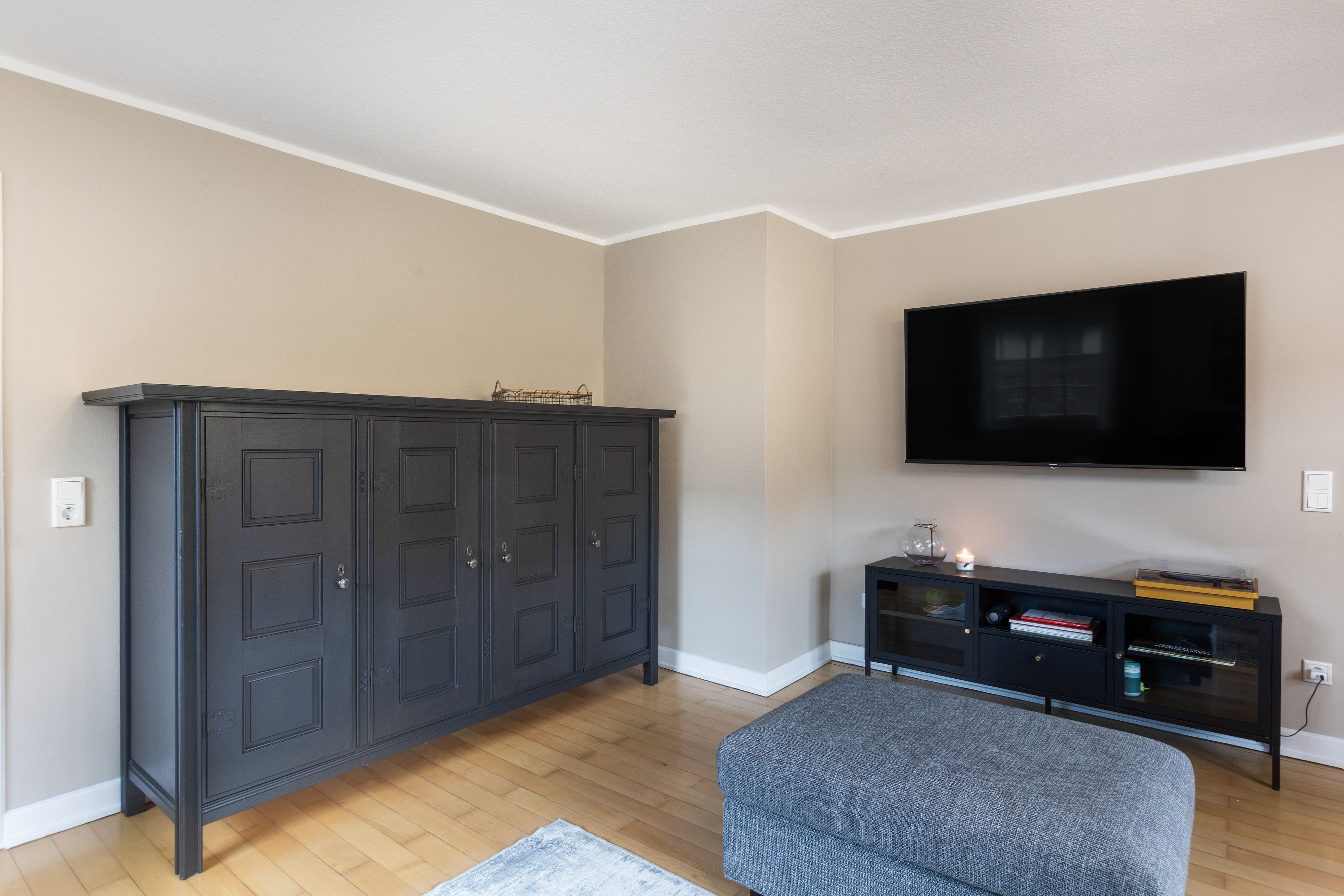 Een kamer met een donkere houten garderobe, een wandgemonteerde flatscreen televisie en een grijs gestoffeerde bank.