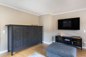 Una habitación con un armario de madera oscura, un televisor de pantalla plana montado en la pared y un banco tapizado en gris.