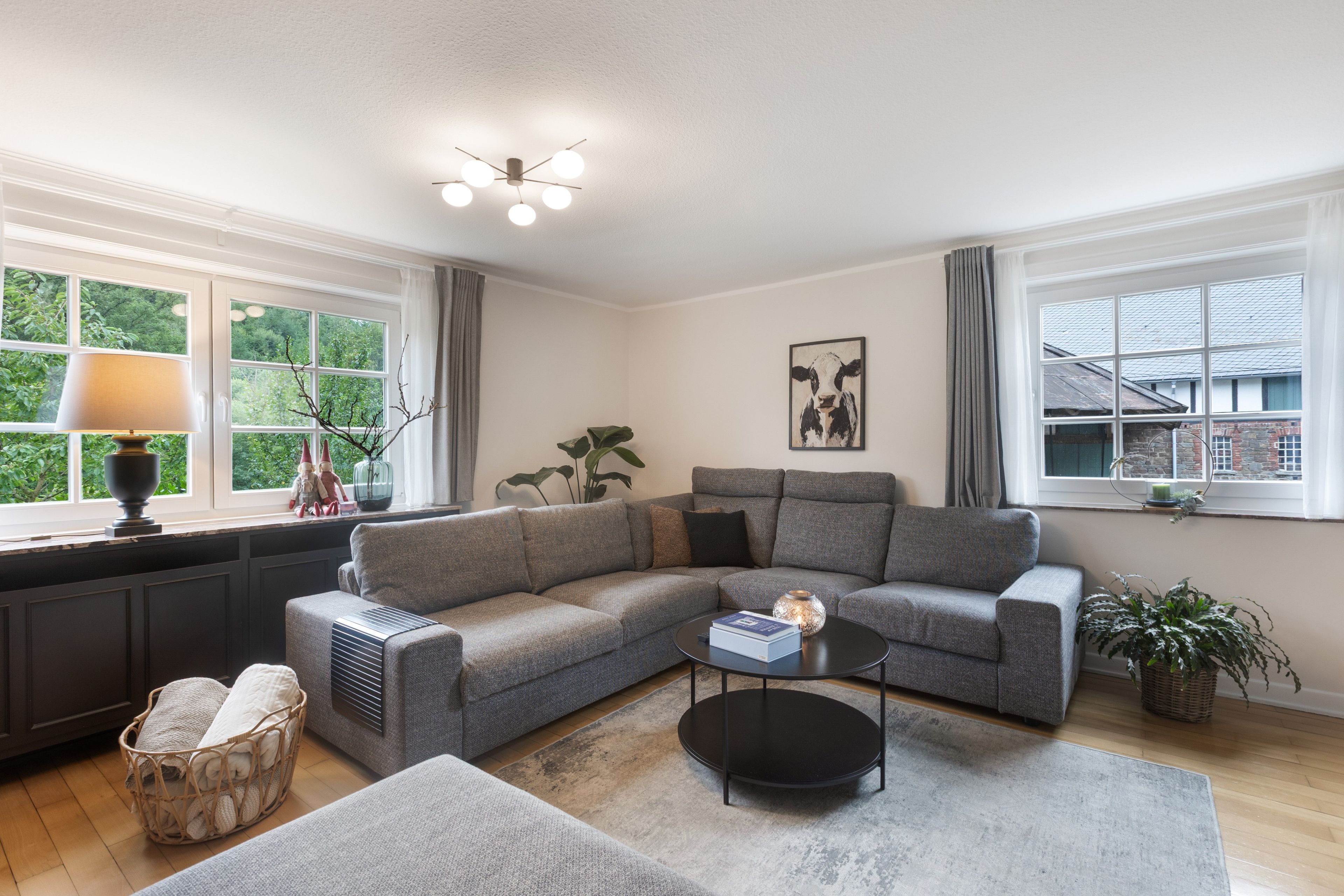 A modern living room with a grey sectional sofa, a black coffee table, a radiator, and a window with curtains.