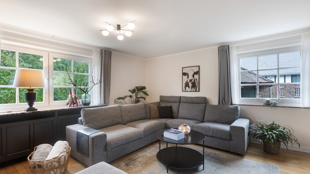 A modern living room with a grey sectional sofa, a black coffee table, a radiator, and a window with curtains.