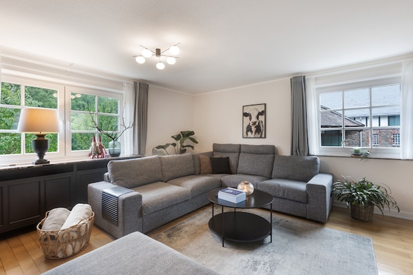 A modern living room with a grey sectional sofa, a black coffee table, a radiator, and a window with curtains.
