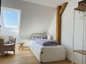 Une chambre à coucher avec un lit, une chaise, une petite table et une fenêtre.