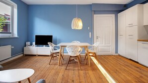 Eine moderne Küche mit Esstisch, Stühlen, einem Fernseher und weißen Schränken.