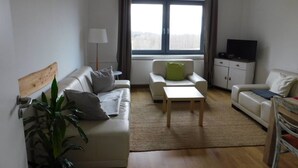 Ett modernt vardagsrum med en soffa, ett litet bord, en tv och en växt.