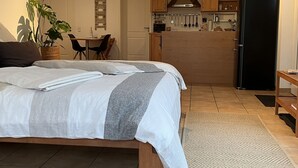 Um quarto com cama, uma mesa de jantar com cadeiras, uma cozinha com armários e uma geladeira.