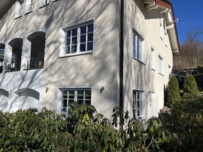 Een gebouw met twee verdiepingen, meerdere ramen, balkons en een verzorgde tuin.