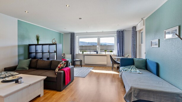 Una sala de estar moderna con sofá, mesa de comedor y vistas amplias a través de grandes ventanales.