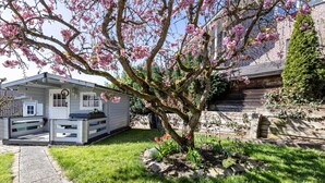 Una casa con jardín, un sendero y un pequeño árbol de flores rosas.