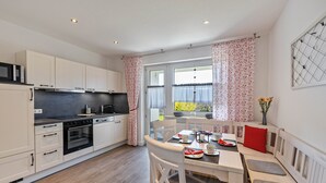 Una cocina moderna con gabinetes blancos, una encimera negra y una zona de comedor con banco y mesa.