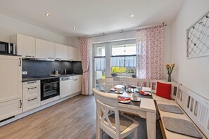 Cozinha moderna com armários brancos, bancada preta e área de jantar com banco e mesa.