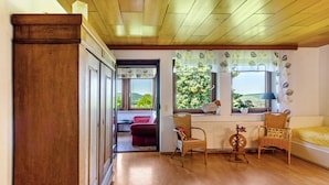 A room with wooden flooring, a wicker chair, a sofa, a radiator, and a window with a view of greenery. - Apartment 'Landleben' with Mountain View and Shared Garden (Hofgeismar)