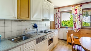 A kitchen with white cabinets, a sink, stove, and a dining area with a table and chairs. - Apartment 'Landleben' with Mountain View and Shared Garden (Hofgeismar)