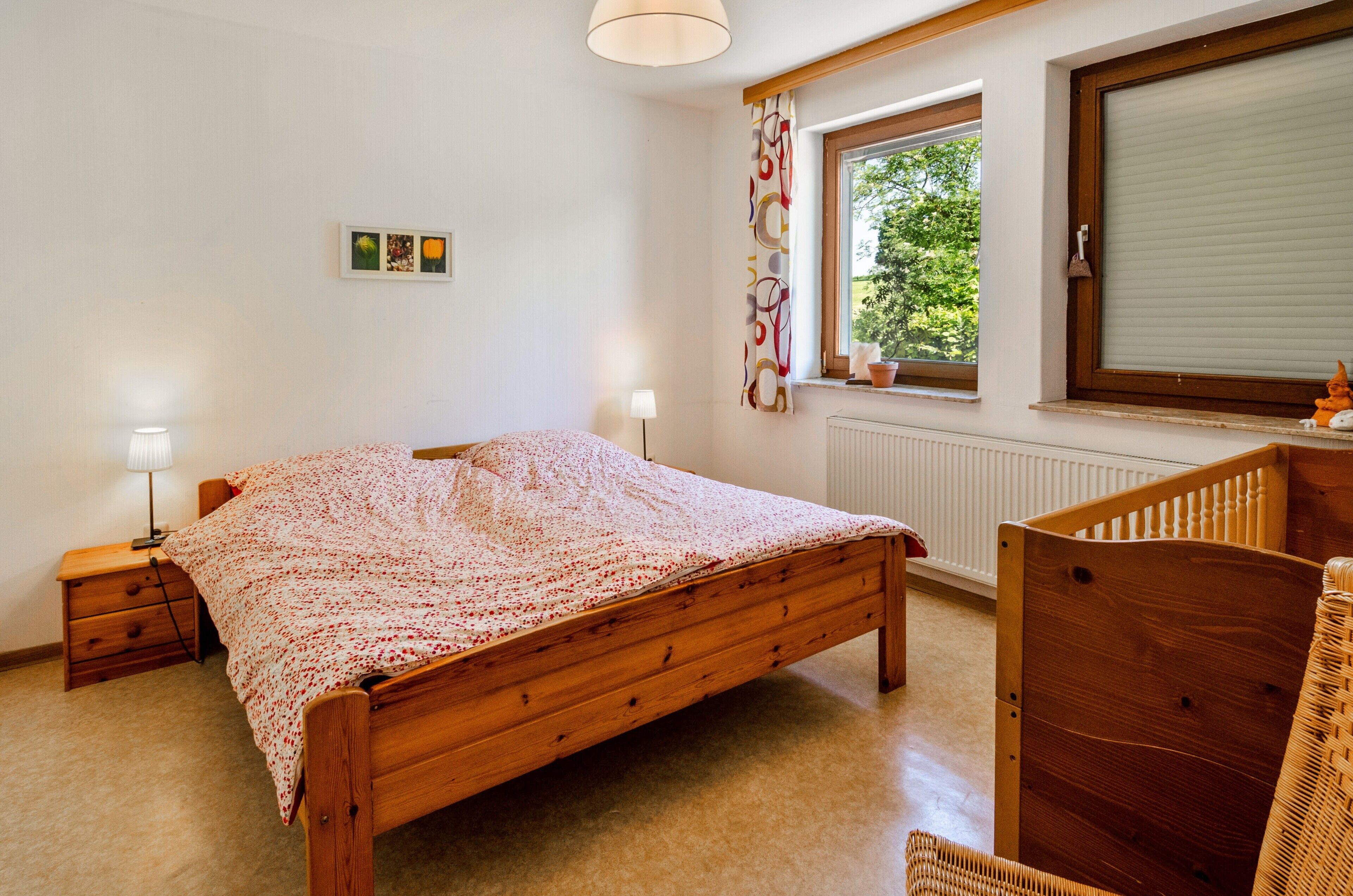 Une chambre à coucher avec un lit en bois, des tables de chevet, une fenêtre avec des rideaux et un radiateur.