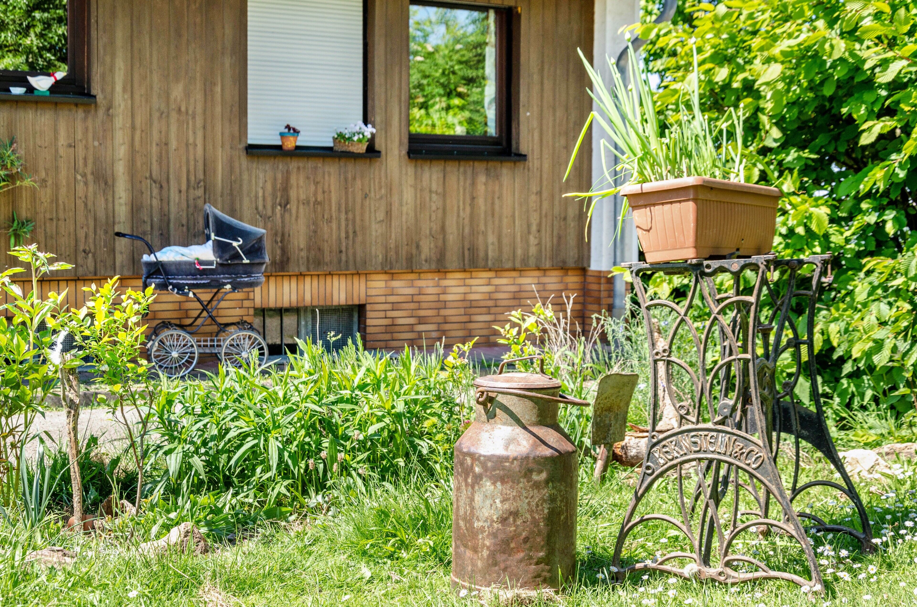 Een tuin met een metalen kar, een fiets en een huis met houten bekleding en ramen.