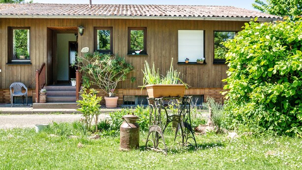 A wooden house with a tiled roof, a front porch, and a garden with potted plants and a metal chair. - Apartment 'Landleben' with Mountain View and Shared Garden (Hofgeismar)