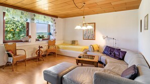 A cozy living room with a sofa, armchair, and a small table. There is a window with a view of greenery outside. - Apartment 'Landleben' with Mountain View and Shared Garden (Hofgeismar)