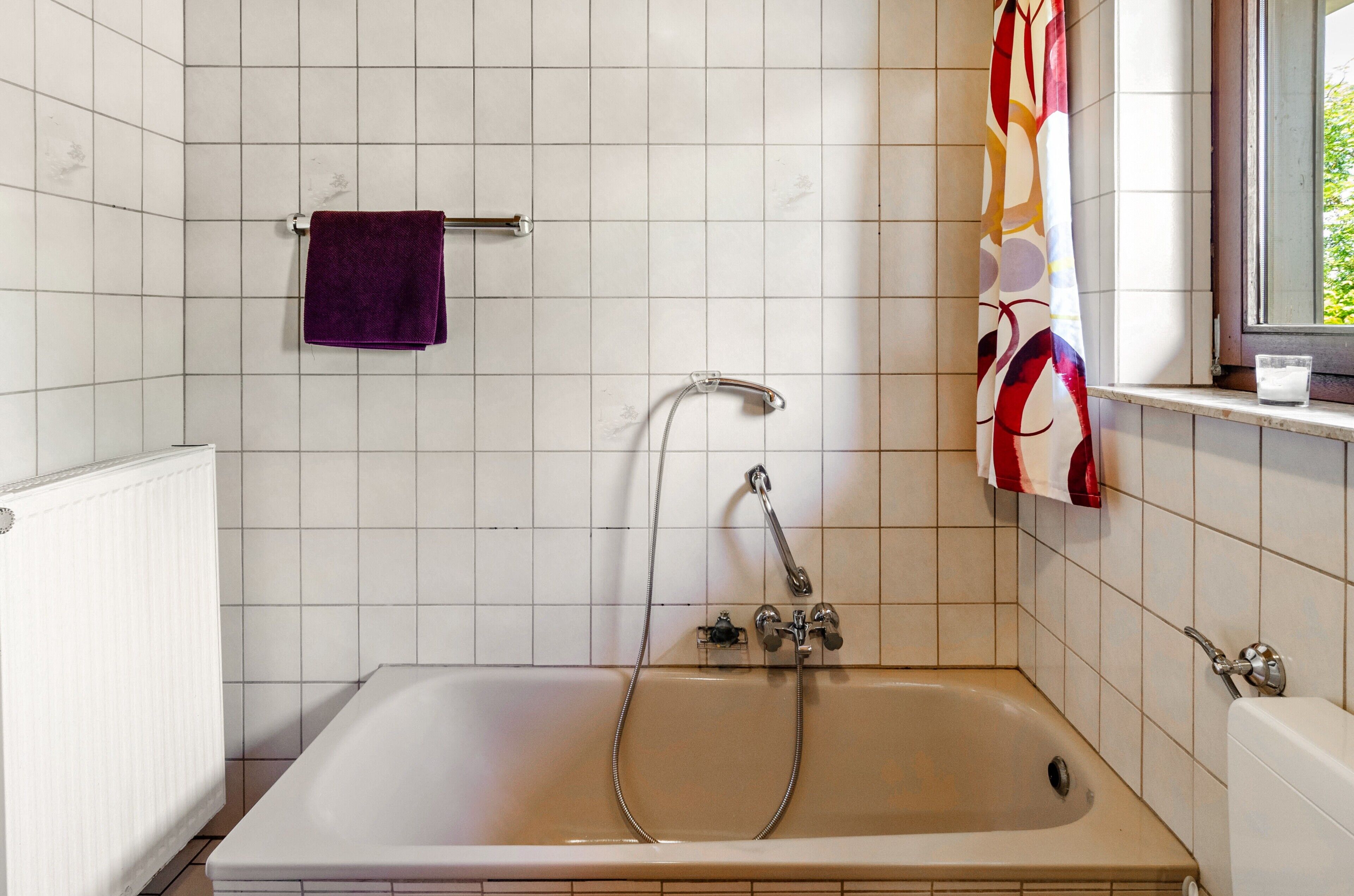 Ein Badezimmer mit einer Badewanne, einem Fenster mit Vorhang und einem Handtuchhalter.