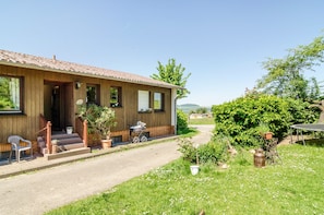 A wooden house with a tiled roof, a porch with steps, and a garden with potted plants and a bicycle. - Apartment 'Landleben' with Mountain View and Shared Garden (Hofgeismar)