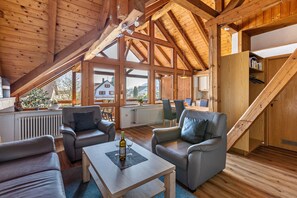 Il s'agit d'une pièce spacieuse de style loft, avec de hauts plafonds, des poutres en bois et de grandes fenêtres. On y trouve des canapés en cuir, une table basse en bois et un escalier menant à un niveau supérieur.