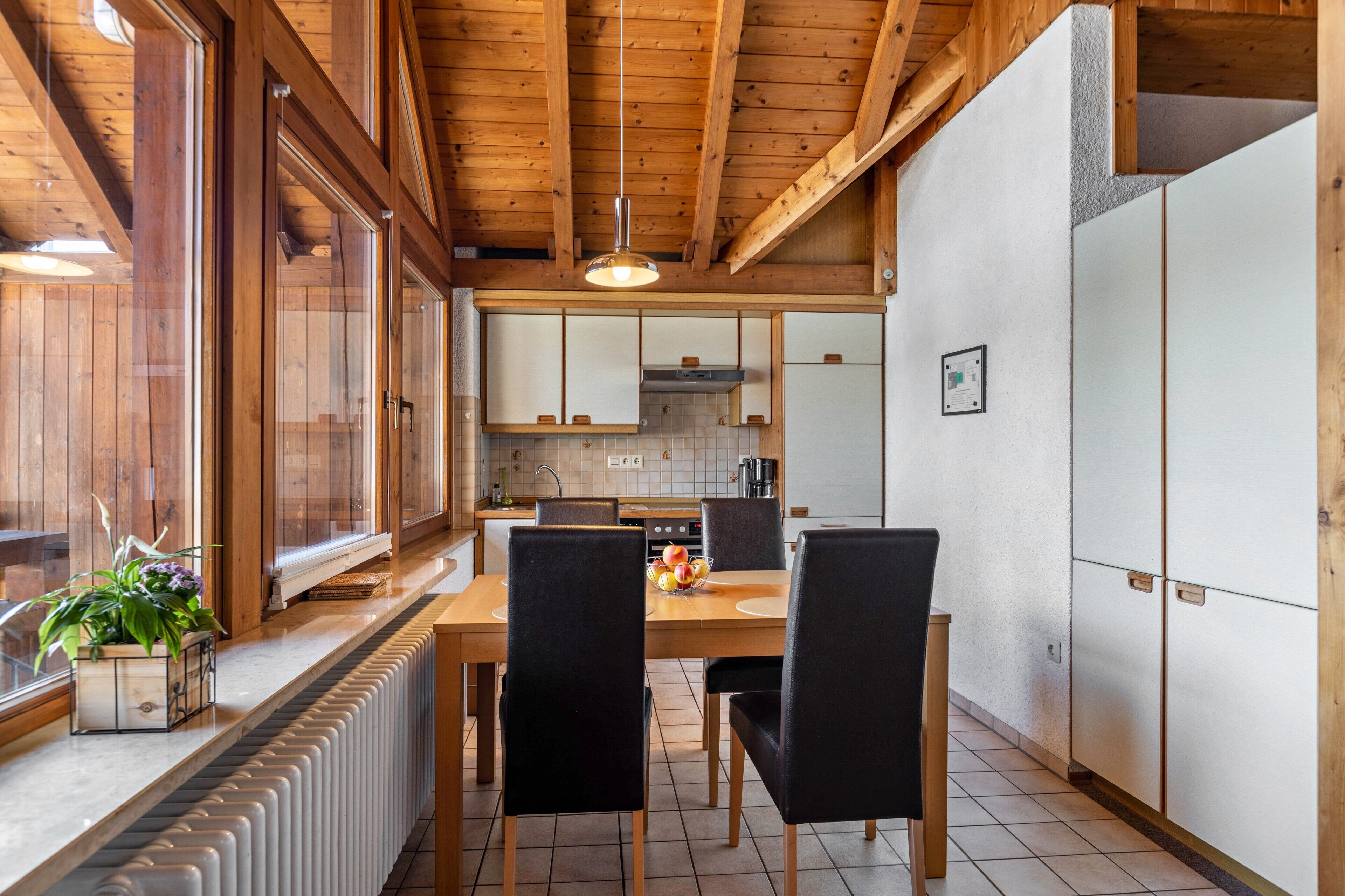 Een houten interieur met een eettafel, stoelen, een radiator en een keuken met kasten en een hanglamp.