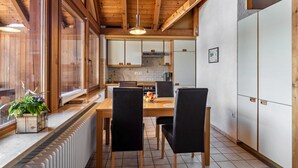 Ein Holzinterieur mit einem Esstisch, Stühlen, einem Heizkörper und einer Küchenzeile mit Schränken und einer Pendelleuchte.