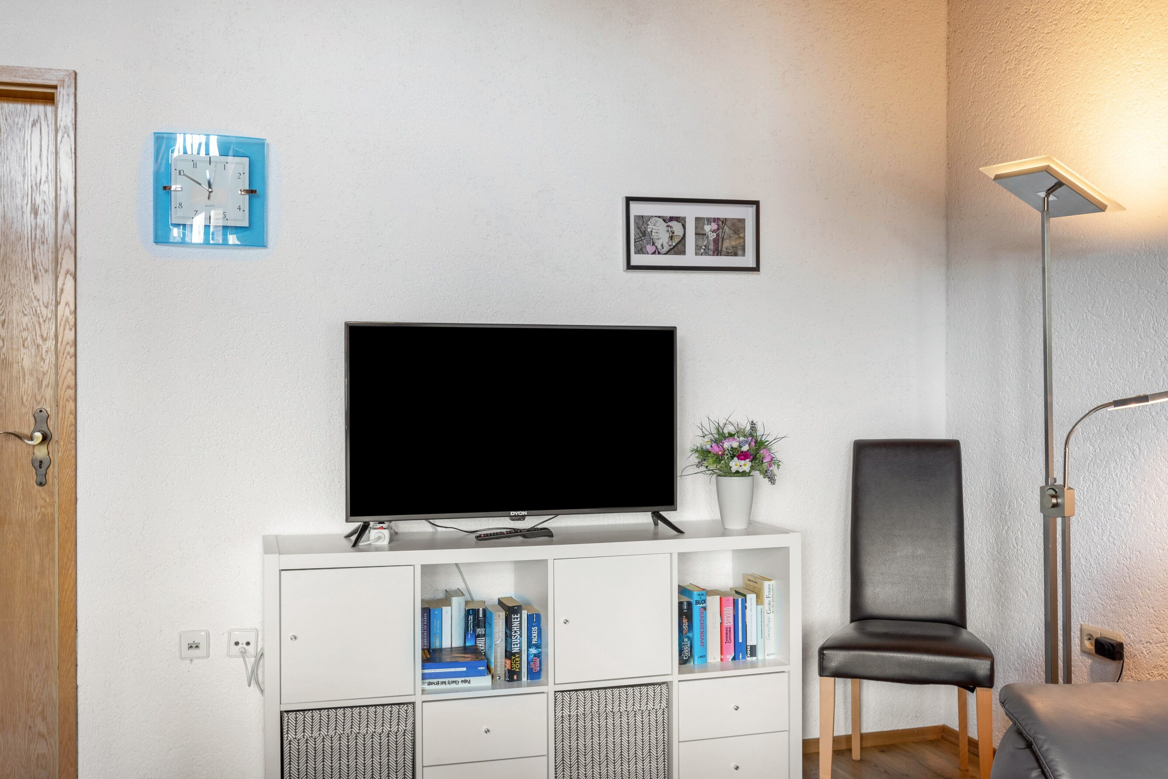 Un salon équipé d’un téléviseur à écran plat, de bibliothèques, d’un fauteuil et d’une horloge murale.
