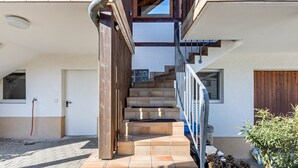 Eine Treppe führt zu einer zweiten Etage, eine Holztür und ein Fenster sind zu sehen.