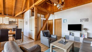 Ein modernes Interieur mit Holzboden, einem Essbereich, einem Wohnzimmer mit Sofas, einem Fernseher und einem Bücherregal.