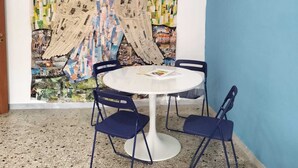 A room with a round white table, four blue chairs, and a large abstract mural on the wall. - Art house - Central station (Napoli)