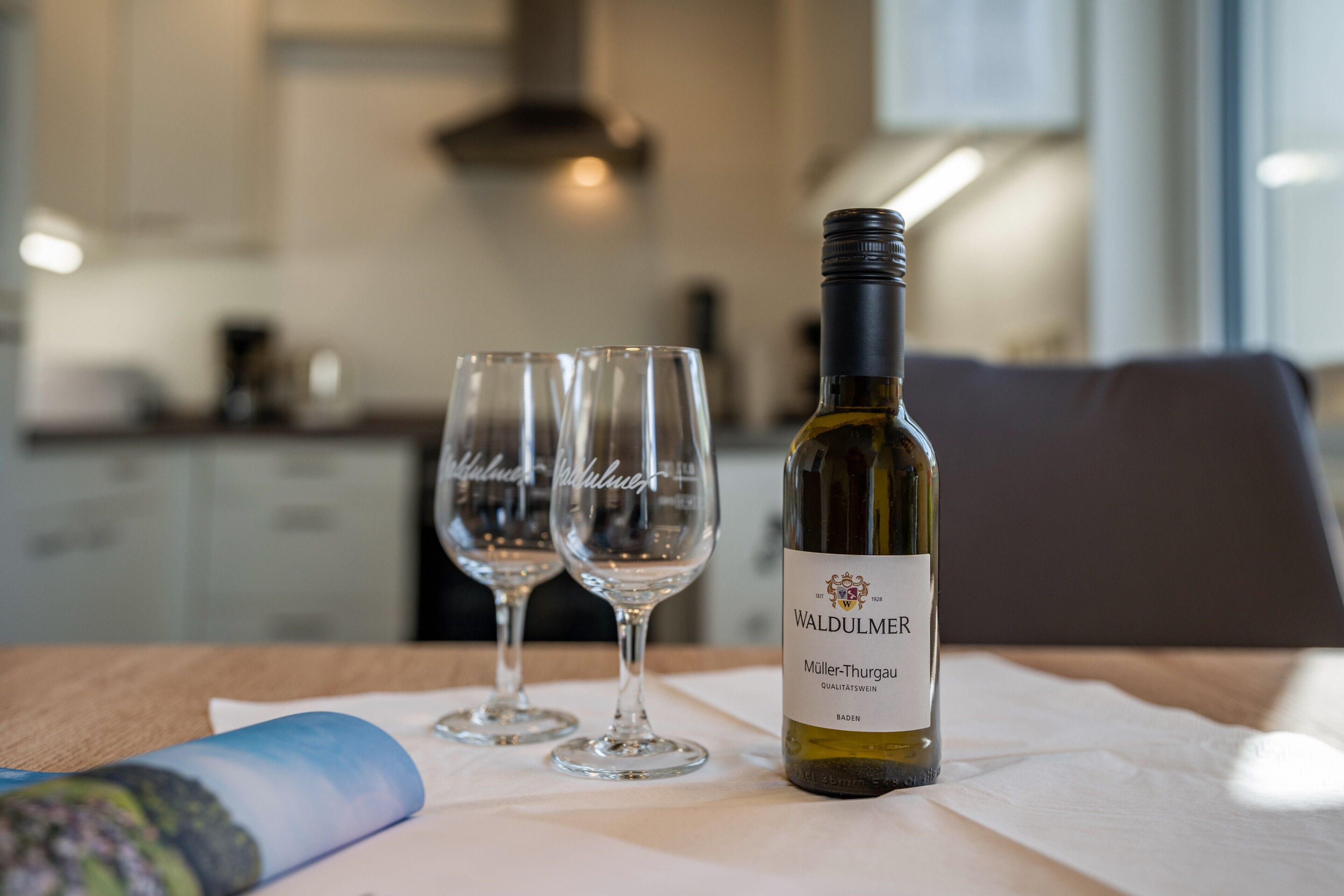 Une bouteille de vin de Waldulmer, deux verres à vin vides et une serviette en papier sur une table dans une cuisine moderne.