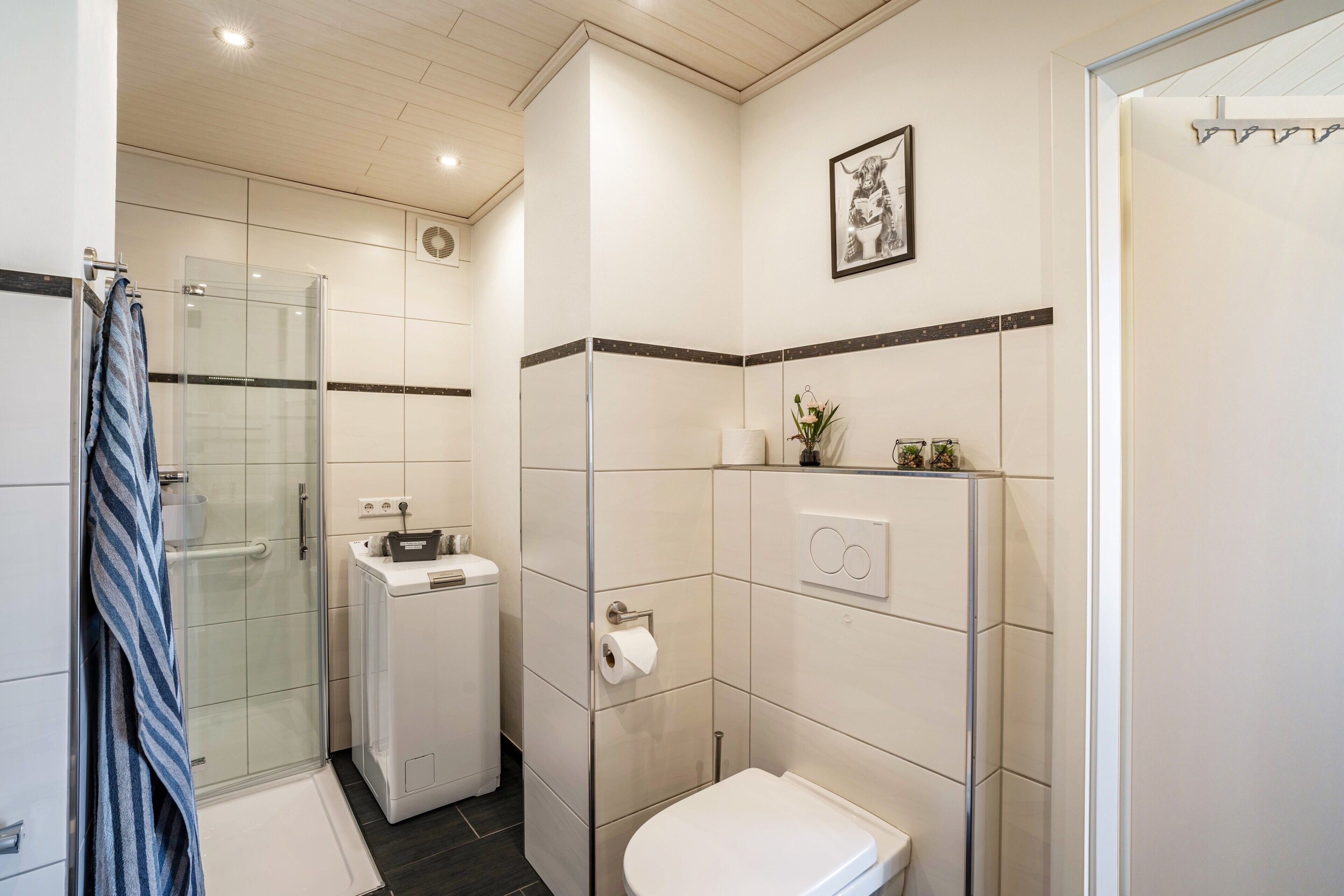 Un baño moderno con cabina de ducha de vidrio, un inodoro blanco y un lavamanos pequeño.