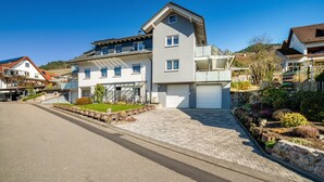 A two-story residential building with a garage, a driveway, and a landscaped garden. - Holiday Apartment 'Huschle' with Private Terrace, Wi-Fi and Air Conditioning (Kappelrodeck)