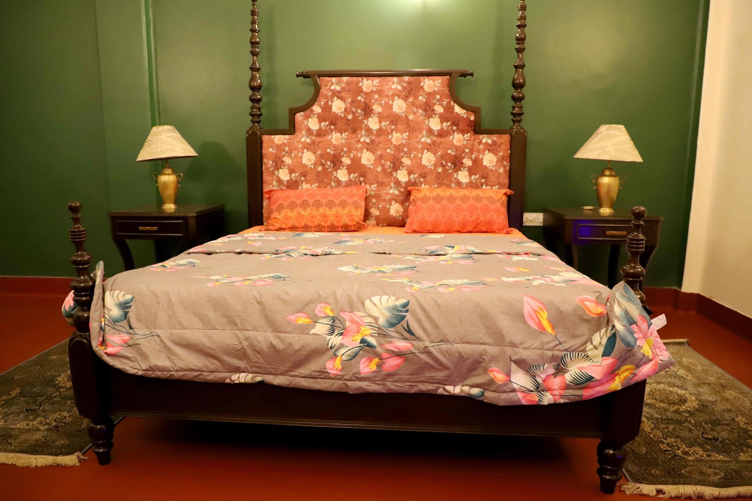 Uma cama com cabeceira florida, duas mesas de cabeceira com abajures e um cobreleito estampado.