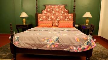 Uma cama com cabeceira florida, duas mesas de cabeceira com abajures e um cobreleito estampado.