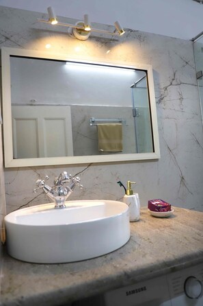 A bathroom with a white sink, a mirror, and a marble backsplash. - Charming 2-bedroom, 2 bath apartment in Central Kolkata with WiFi, AC, Kitchen (Kolkata)