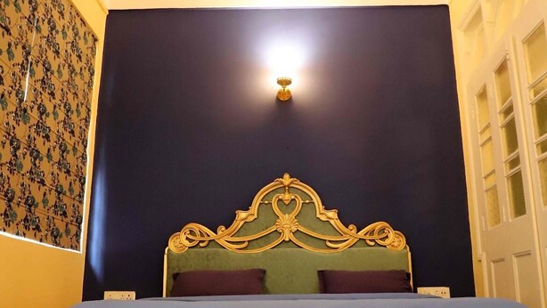A bedroom with a bed, a ceiling fan, a wall-mounted light, and a patterned rug.