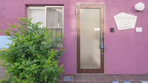 A pink building with a wooden door and a window. There is a sign on the wall that reads "HOTEL KOKORO".