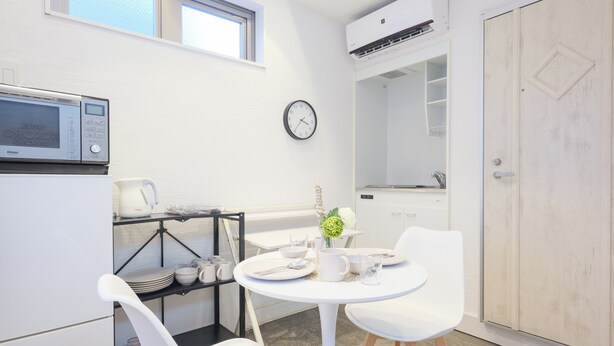 A compact kitchen with a microwave, a clock, and a dining area with chairs and a table.