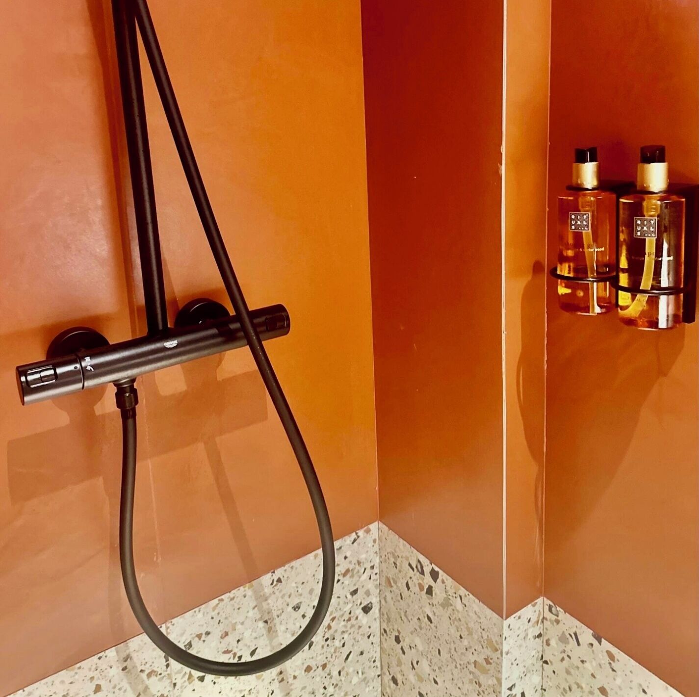 A shower area with a handheld showerhead and a wall-mounted control panel.