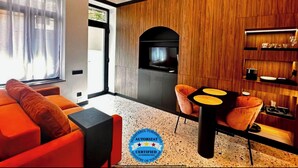 Una sala moderna con un sofá, una mesa de centro y un televisor. Se aprecia una pared de madera y una zona de cocina con un microondas.