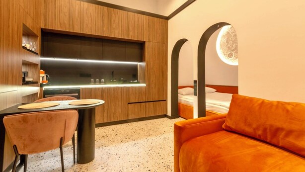 Una habitación de hotel moderna con un muro decorativo de madera, una mesa redonda de comedor con dos sillas, un sofá y una cama con una lámpara circular colgante.