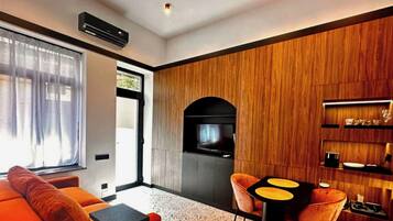 Una sala moderna con un sofá, una mesa de centro y un televisor. Se aprecia una pared de madera y una zona de cocina con un microondas.