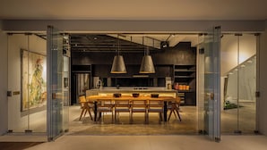 An open-plan space with a central dining table, pendant lighting, and a kitchen area visible through glass doors. - Mandala Oasis (Bali)