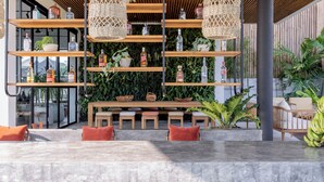 A modern outdoor seating area with a pool, wooden tables, and chairs, surrounded by shelves with bottles and plants. - Mandala Oasis (Bali)